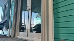 Una escalera conduce a una puerta con paneles de vidrio, un porche con una silla y una pared exterior color turquesa.