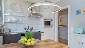 Cocina moderna con armarios blancos, encimera de madera, un bol de limones y hierbas, y una lámpara colgante.