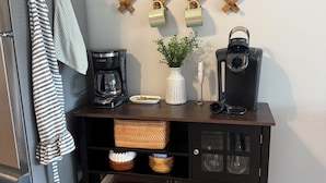 Une cuisine avec un plan de travail en bois foncé, une machine à café, une bouilloire et un porte-épices fixé au mur.