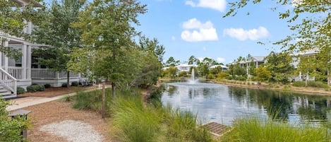 A serene outdoor area with a pond, a fountain, and a pathway leading to a building with a porch.