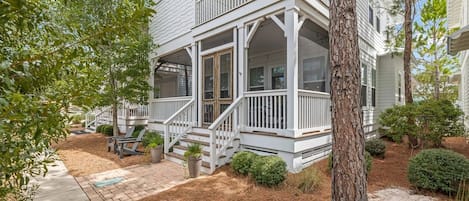 A two-story house with a covered porch, a front yard with a tree, and a brick pathway.
