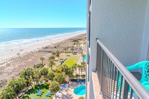 Un balcón con vistas a una playa, una piscina y un área cercada con palmeras.