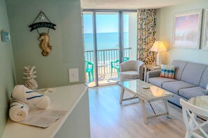 Un salon comprenant un canapé, une table basse en verre, un fauteuil, un panneau d’accueil, une décoration à thème ananas et une vue sur l’océan par une porte coulissante.