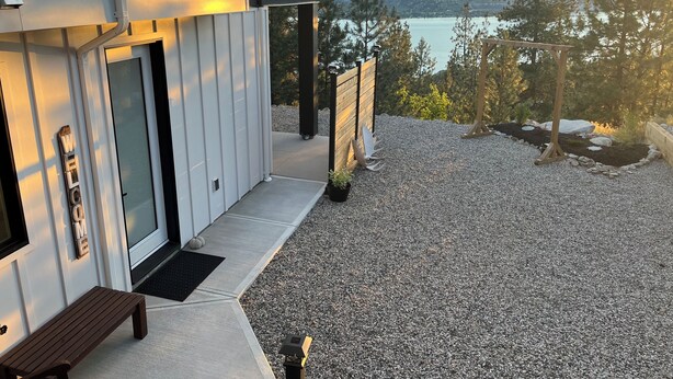 Een modern huis met een grindpad, een bankje en uitzicht op een meer en bergen.