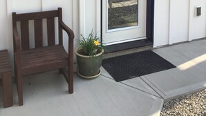 Een witte buitenmuur met een schuifdeur, een houten bankje en een bloempot.