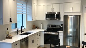 Een moderne keuken met witte kastjes, roestvrijstalen apparatuur, een zwarte eettafel en een raam met zonwering.