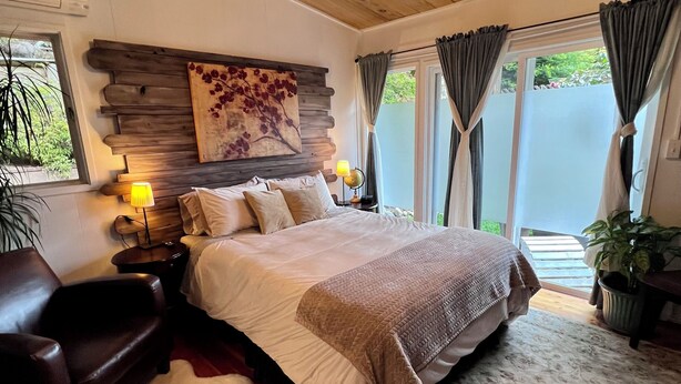 Una camera da letto con un letto grande, soffitto in legno e un lampadario. Si nota un comodino con una lampada, una poltrona in pelle e un tappeto.
