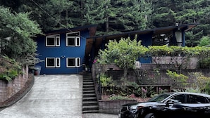 Una casa moderna a due piani con facciata blu, vialetto in cemento e un'auto nera parcheggiata davanti.