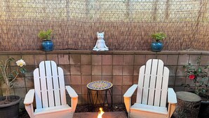 Un patio con due poltrone Adirondack, un tavolino rotondo e un braciere.