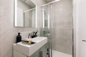 Een moderne badkamer met een douchecabine van glas, een wit wastafelmeubel met een zeepdispenser en een spiegel boven het wastafelmeubel.