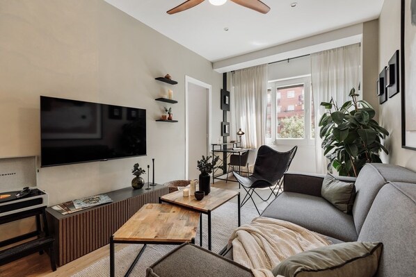 Een moderne woonkamer met een flatscreen televisie, een houten salontafel, een leren fauteuil en een grijze bank.