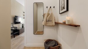 A modern bathroom with a large mirror, a towel hanging on hooks, a shelf with candles, and a wicker basket. - Holzer - 2 bedrooms in Sant Antoni (Barcelona)
