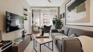 A modern living room with a sofa, a coffee table, a TV, and a ceiling fan. - Holzer - 2 bedrooms in Sant Antoni (Barcelona)