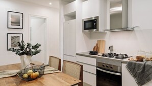 A modern kitchen with white cabinets, a microwave, a stove, and a dining area with a table and chairs. - Holzer - 2 bedrooms in Sant Antoni (Barcelona)