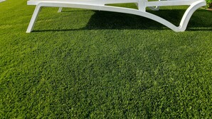 Une chaise longue blanche est posée sur une pelouse bien entretenue, avec un bâtiment en arrière-plan.