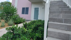 Un immeuble de deux étages avec une façade rose et blanche, un balcon doté de balustrades blanches et un escalier menant à l’étage supérieur.