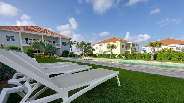 Un espace aménagé au bord de la piscine, avec des chaises longues blanches et une pelouse bien entretenue.