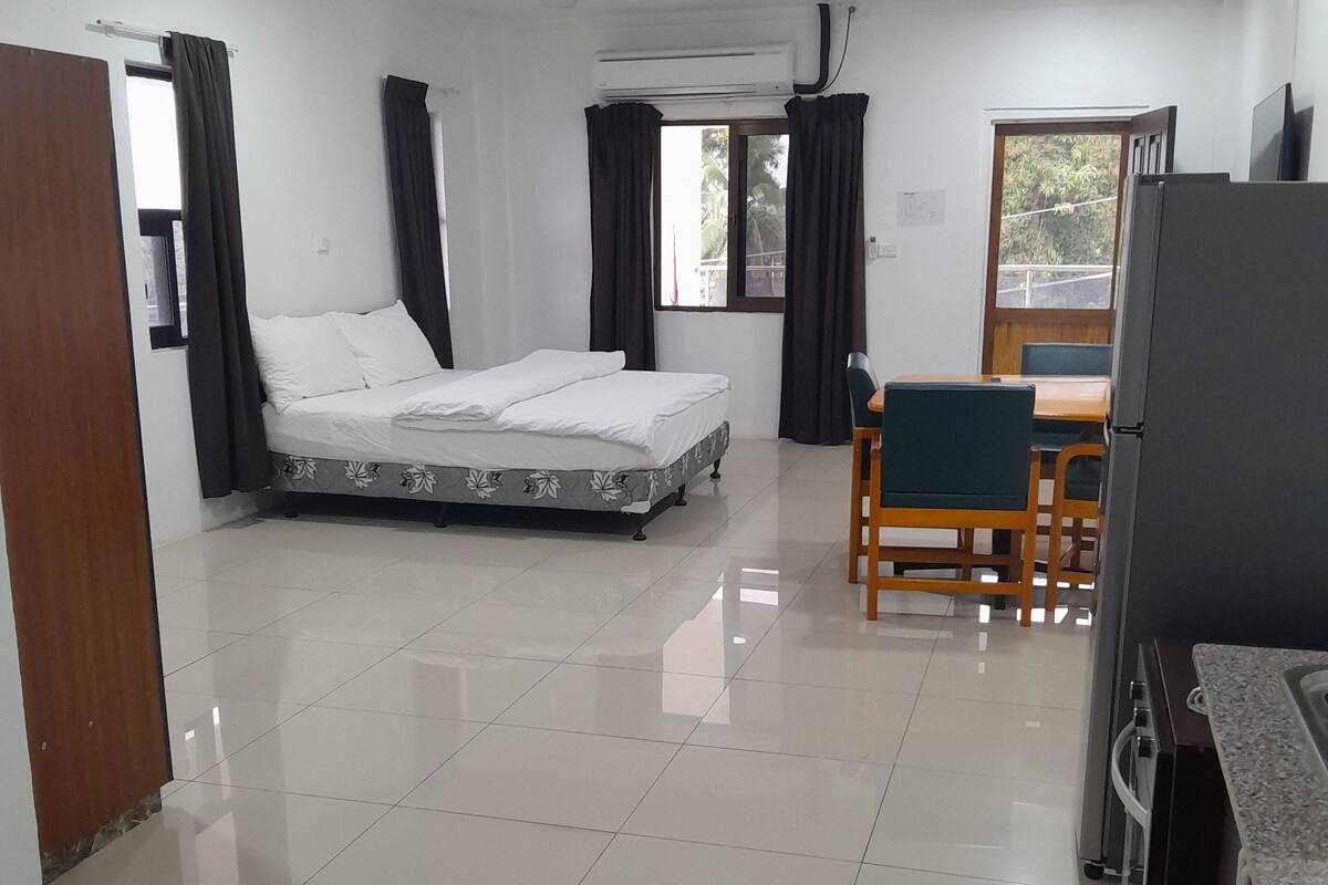 A hotel room with a bed, a dining table with chairs, a refrigerator, and a window with curtains.