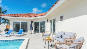 Zona de piscina con sillones, un sofá de mimbre y una pequeña mesa con bebidas.