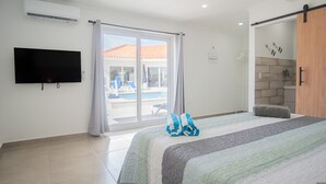 Habitación de hotel con una cama grande, un televisor de pantalla plana, una puerta corrediza de vidrio a un área de piscina y un armario de madera.
