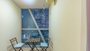 En lille balkon med et bord og to stole, et stort vindue med udsigt over bybilledet og en loftlampe.