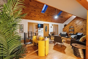 Una sala de estar acogedora con suelo de madera, techo alto con tragaluces y una combinación de sofás amarillos y grises.