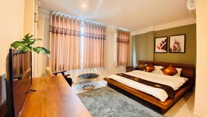 A hotel room with a wooden bed, a desk, a chair, a TV, and a plant. - Trieu Nguyen Hotel (Ho Chi Minh City)