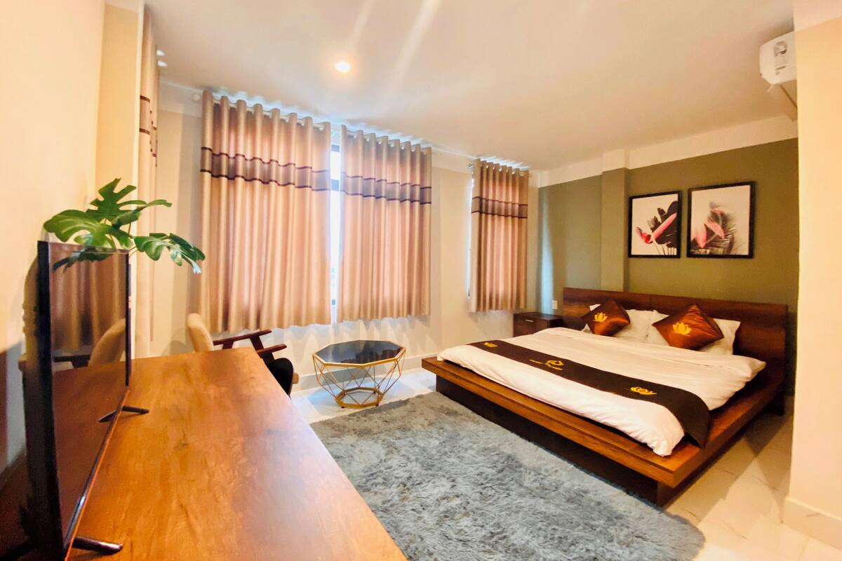 Habitación de hotel con una cama de madera, un escritorio, una silla, un televisor y una planta.