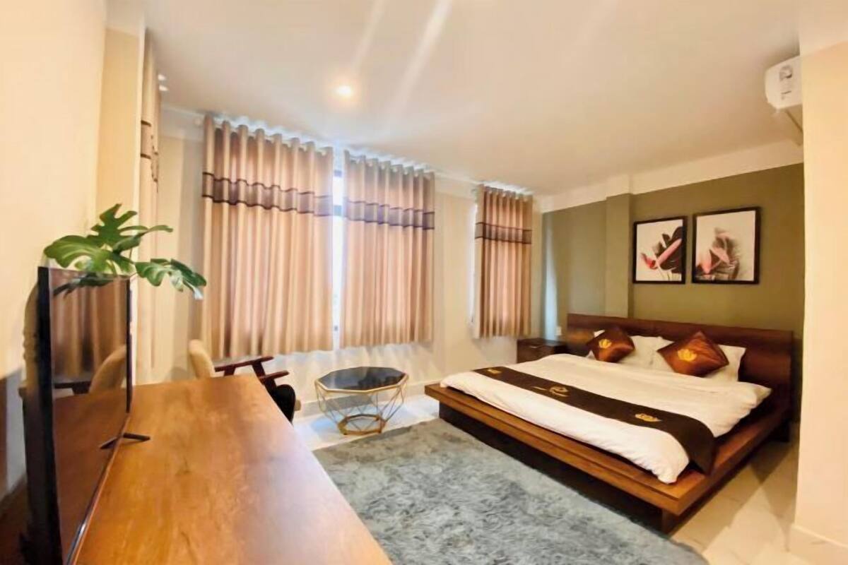 Una habitación de hotel con cama, escritorio, silla, una mesita y una planta.