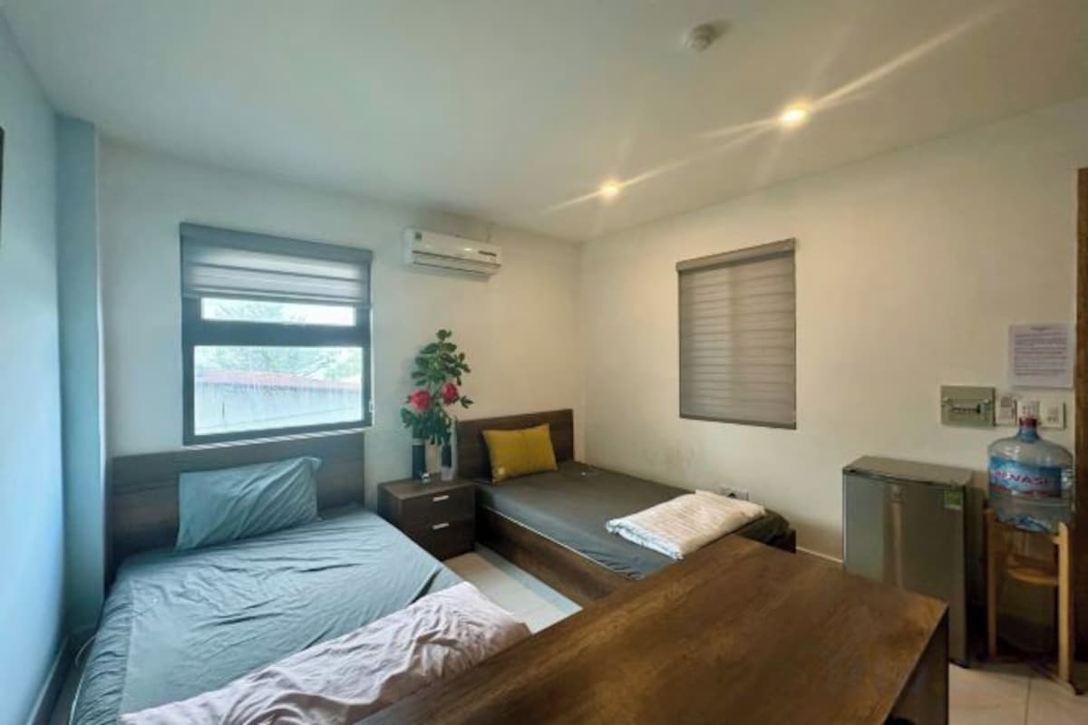 Habitación de hotel pequeña con cama, un escritorio, una silla, un ventanal y un dispensador de agua.