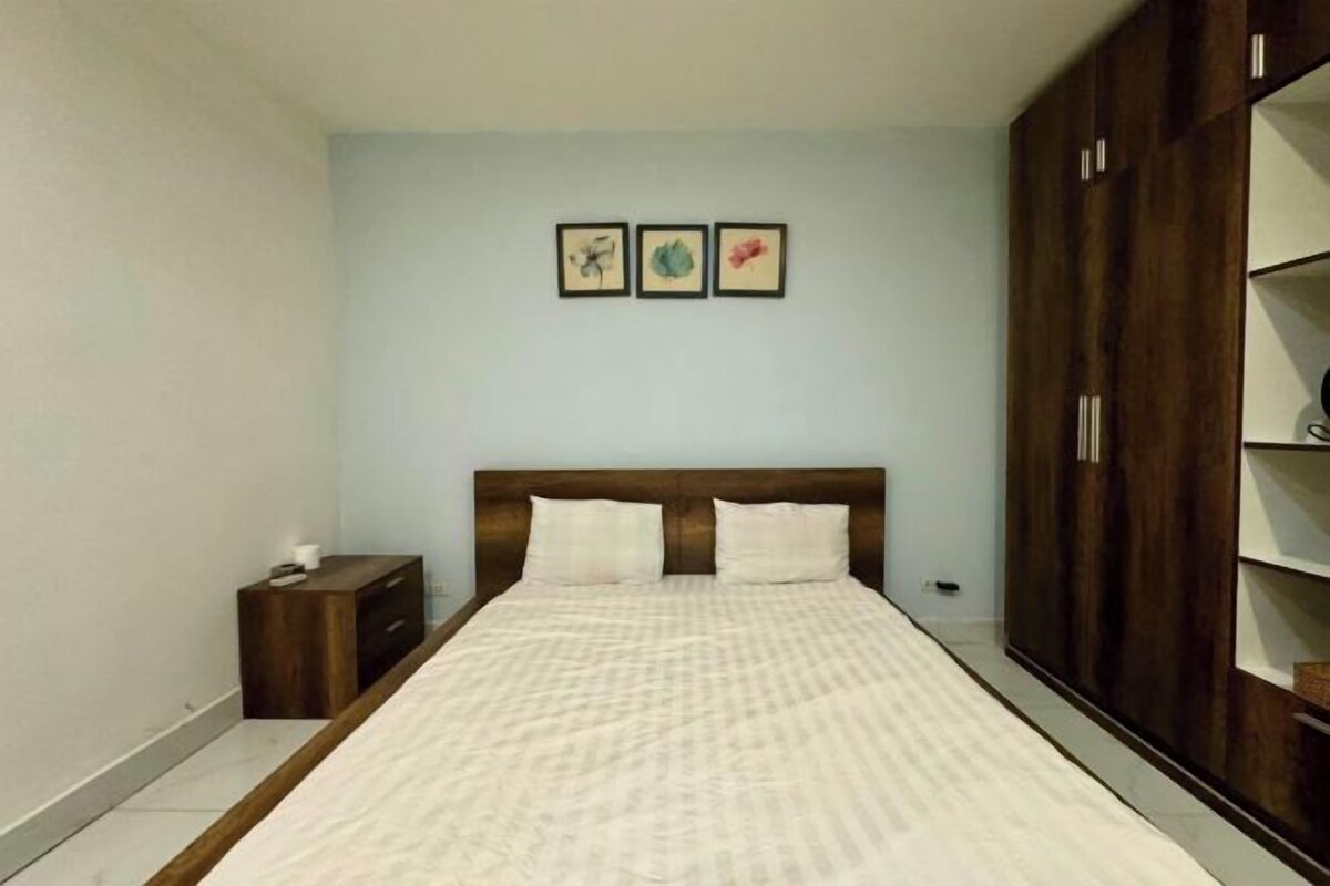 Quarto com cama, mesa de cabeceira, guarda-roupa e três quadros na parede.