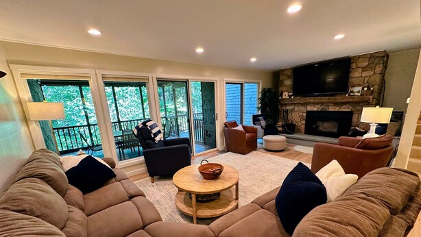 A living room with a sectional sofa, a fireplace, and a balcony with a view of trees. - A1 Luxury Bretton Woods Ski-in Ski-out Townhome Next to Beginner ski Area Fast Wifi Keyless Entry (Bretton Woods)