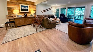 A spacious living area with a wooden accent wall, a large window with a view, and a cozy seating arrangement. - A1 Luxury Bretton Woods Ski-in Ski-out Townhome Next to Beginner ski Area Fast Wifi Keyless Entry (Bretton Woods)