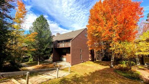 A modern two-story house with a balcony, surrounded by autumn foliage and a well-maintained lawn. - A1 Luxury Bretton Woods Ski-in Ski-out Townhome Next to Beginner ski Area Fast Wifi Keyless Entry (Bretton Woods)