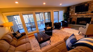 A cozy living room with a sectional sofa, a coffee table, and a fireplace. There is a balcony with outdoor furniture visible through the glass doors. - A1 Luxury Bretton Woods Ski-in Ski-out Townhome Next to Beginner ski Area Fast Wifi Keyless Entry (Bretton Woods)