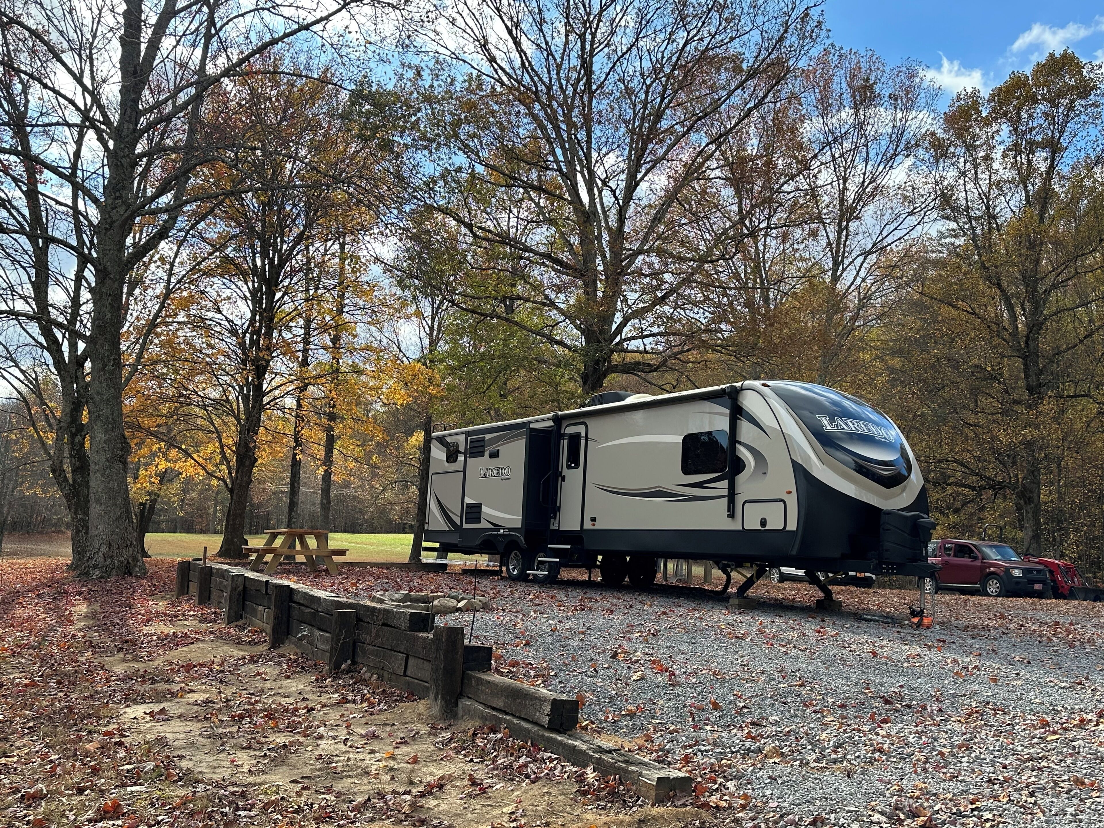 Un camper parcheggiato in una zona boschiva con un vialetto sterrato e tavoli da picnic.