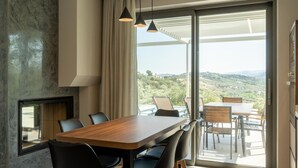 Un comedor moderno con una mesa y sillas de madera, ventanas amplias con vistas al campo y luminarias colgantes.
