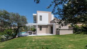 Una casa moderna con un patio cubierto, una piscina y un césped cuidado.