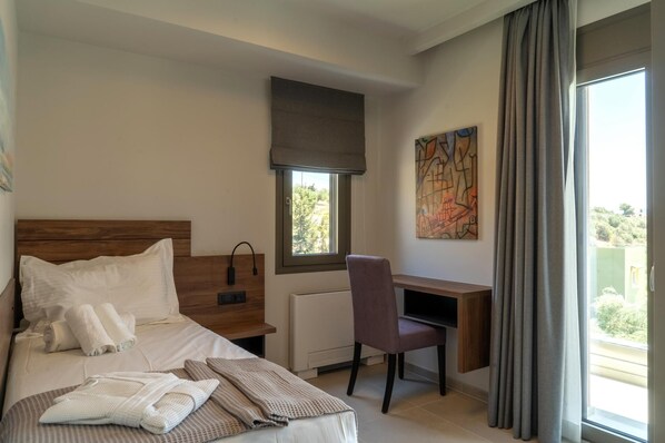 A hotel room with a bed, a desk, a chair, a window with a view, and a painting on the wall. - Anthemis Luxury Villas 2 (Heraklion)