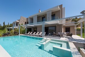 A modern two-story house with a swimming pool, outdoor seating, and a stone facade. - Anthemis Luxury Villas 2 (Heraklion)