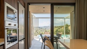 A modern kitchen with a built-in oven and a glass door leading to a balcony with a dining table and chairs, overlooking a scenic landscape.