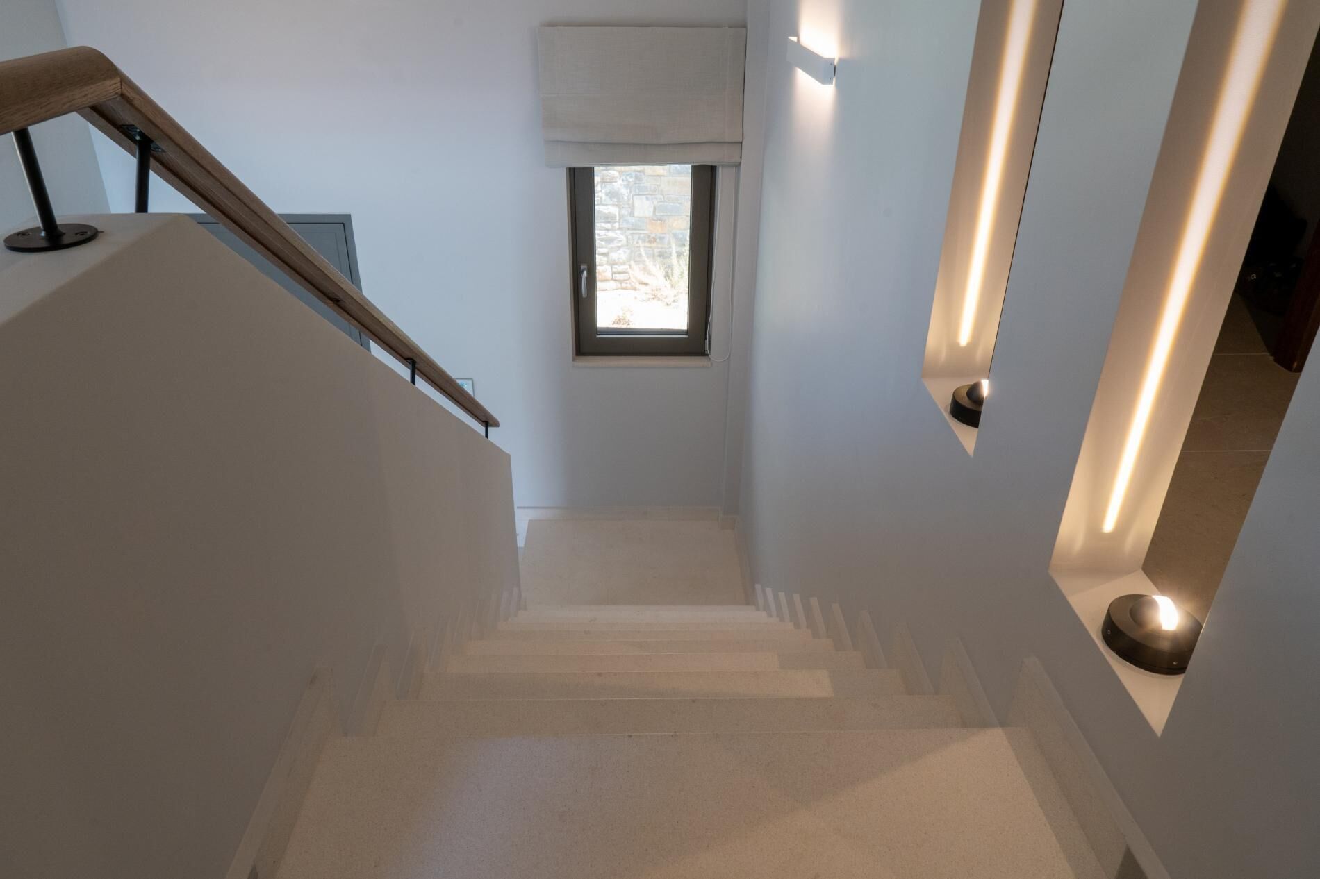 Un escalier avec une rampe en bois, une petite fenêtre donnant sur le paysage et un luminaire fixé au mur.