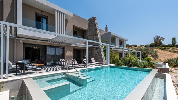 A modern poolside area with a clear pool, lounge chairs, and a stone pillar.