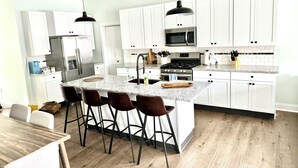 A modern kitchen with white cabinets, stainless steel appliances, a granite countertop, and a central island with bar stools. - Heart of Convenience Downtown near Convention Center-Lucas Oil-Fully Remodeled  (Indianapolis)