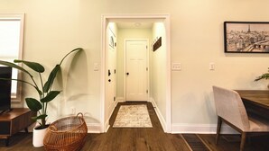 A hallway with a white door, a small rug, a wicker basket, and a chair. - Heart of Convenience Downtown near Convention Center-Lucas Oil-Fully Remodeled  (Indianapolis)