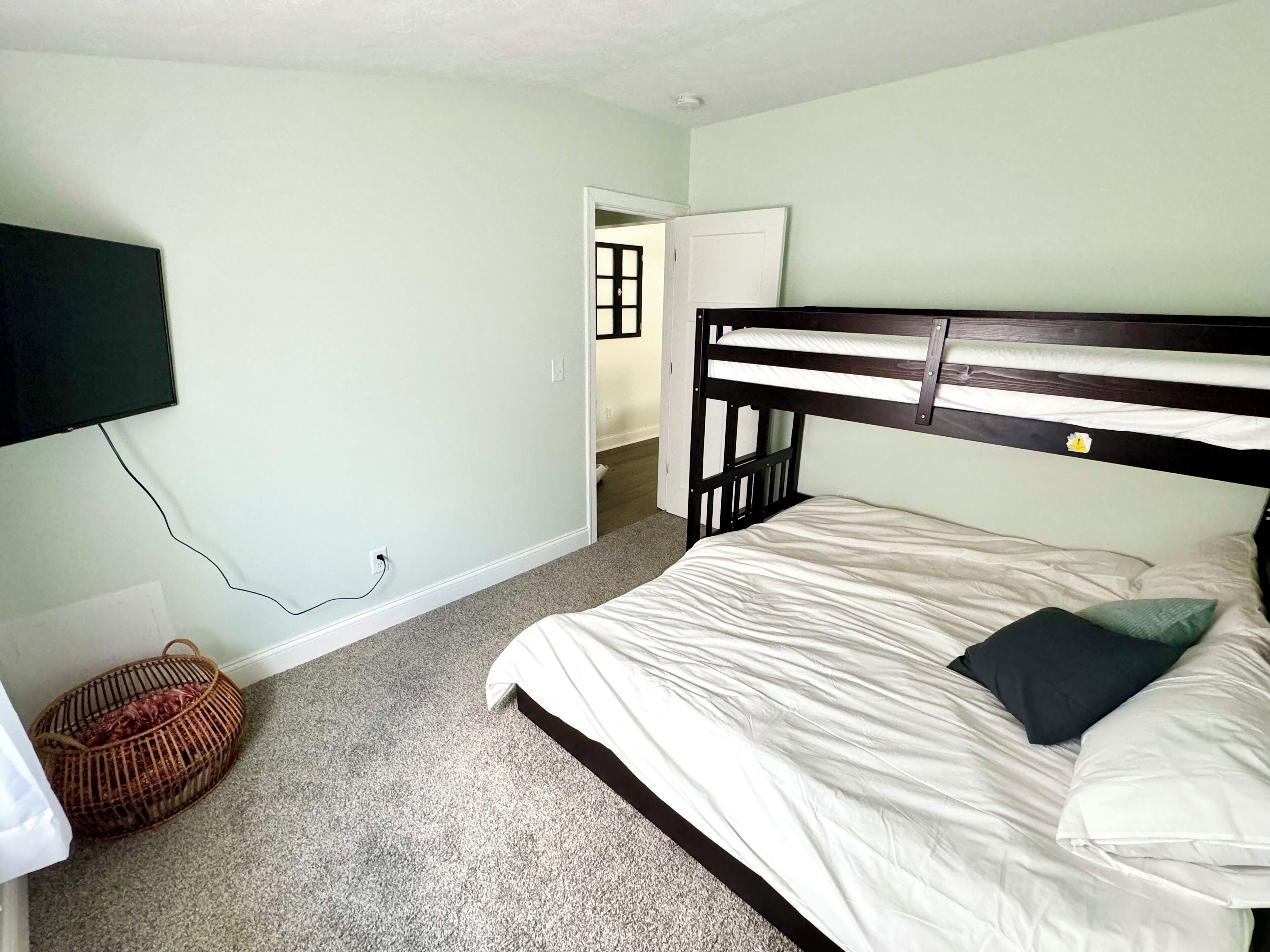 A bedroom with a bunk bed, a television mounted on the wall, a carpeted floor, and a door leading to another room.