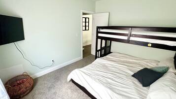 A bedroom with a bunk bed, a television mounted on the wall, a carpeted floor, and a door leading to another room.