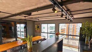A modern interior with a long dining table, large windows, and industrial ceiling elements. - AX Way Tambaú Suítes (João Pessoa)