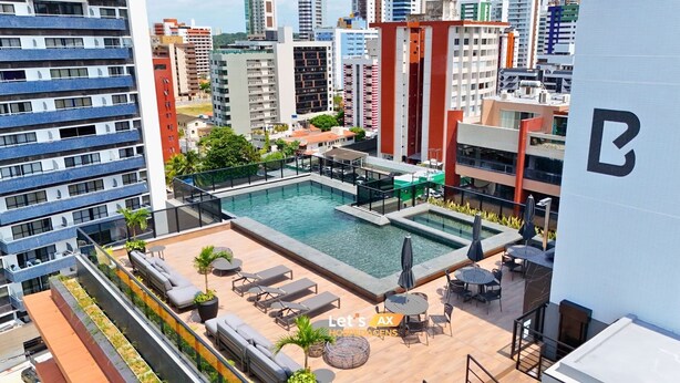 A rooftop pool area with lounge chairs and umbrellas, surrounded by high-rise buildings. - AX Way Tambaú Suítes (João Pessoa)
