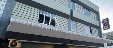 A multi-story building with a flat facade, large windows on the ground floor, and a sign indicating it is a guest house.
